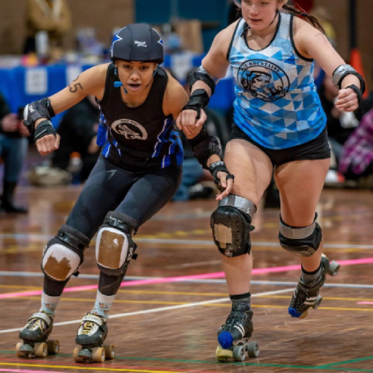 Two skaters from opposing teams skating forwards on a wooden surface